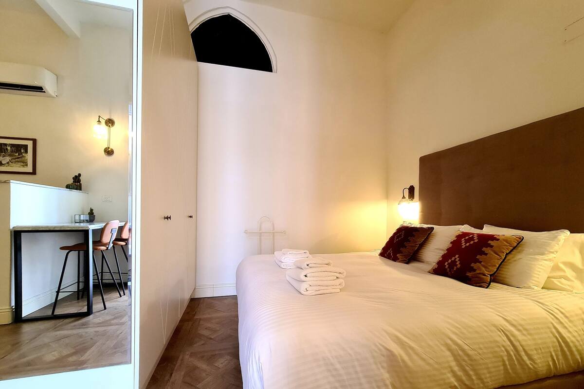 A bedroom with a bed, bedside lamps, and a small desk with chairs.