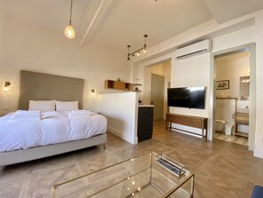A modern hotel room with a large bed, a TV, a small desk, and a glass coffee table. - Kubler's House-  By Beach Apartments TLV (Tel Aviv)