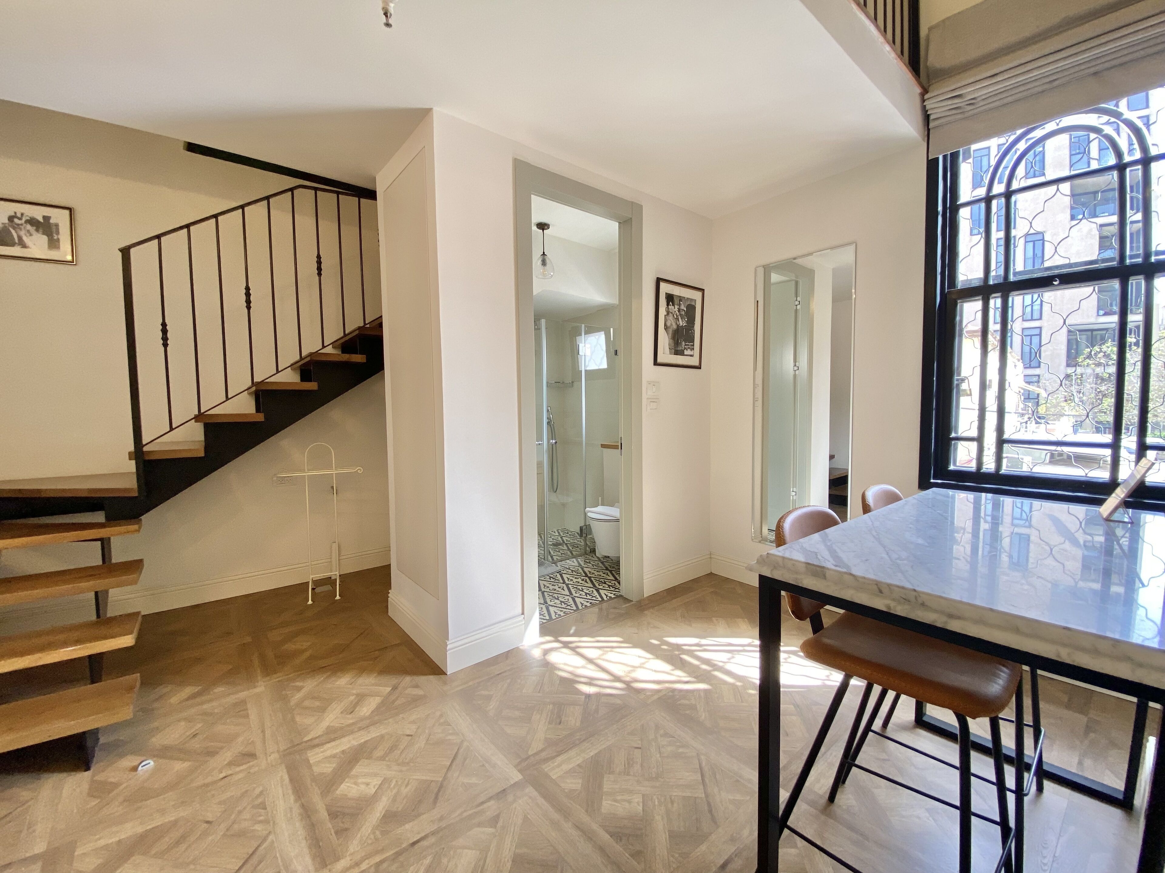 Un intérieur moderne avec un escalier en bois, une salle de douche en verre et un coin repas doté d’une table en marbre.