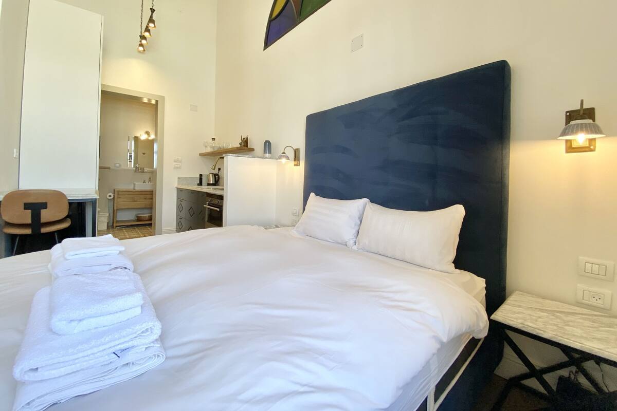 A hotel room with a large bed, a desk, a chair, a small kitchen area, and a bathroom.