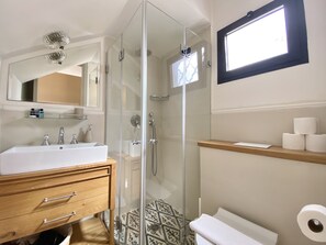 A modern bathroom with a glass-enclosed shower, a wooden vanity with a sink, and a toilet with a roll of toilet paper on the wall. - Kubler's House-  By Beach Apartments TLV (Tel Aviv)