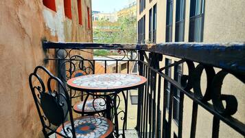 A small outdoor balcony with a round table and two chairs, surrounded by a metal railing.