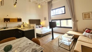 A modern hotel room with a bed, a sofa, a dining table, a kitchen area, and a large window with curtains. - Kubler's House-  By Beach Apartments TLV (Tel Aviv)