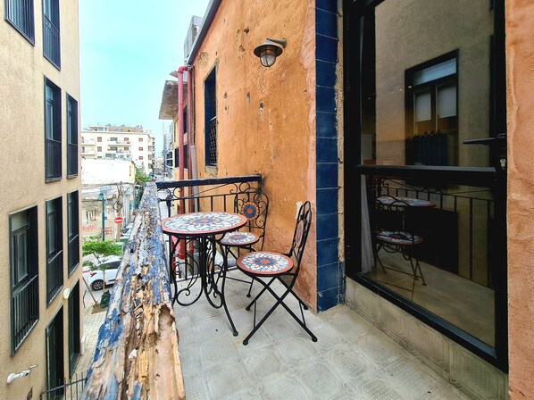 A balcony with a tiled table and chairs, a view of the street, and a building with a textured wall. - Kubler's House-  By Beach Apartments TLV (Tel Aviv)