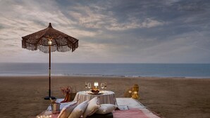 A beachside dining setup with a table, pillows, a blanket, and a decorative umbrella. - Larisa Resort, Morjim (Morjim)