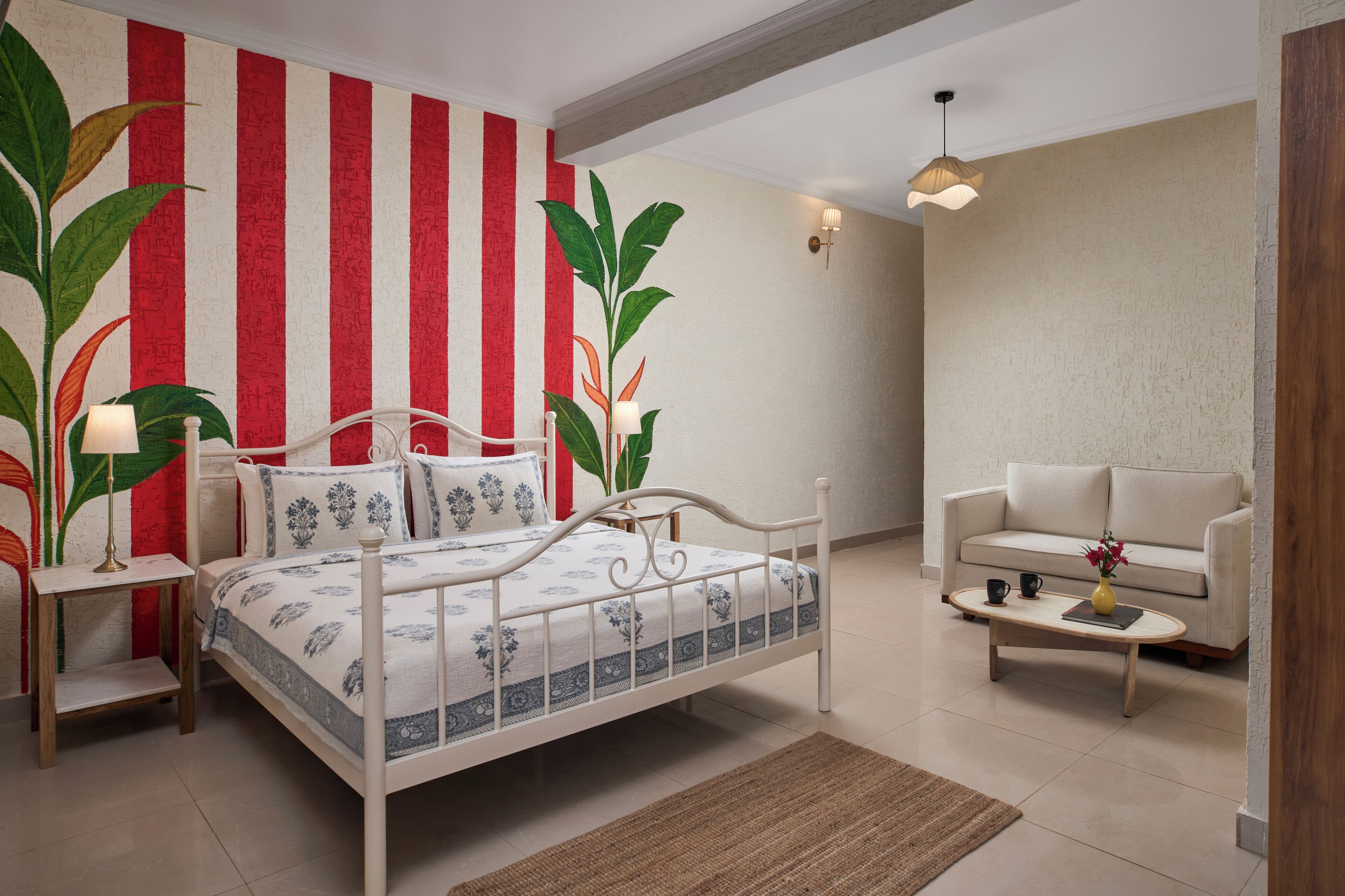 A bedroom with a bed, bedside tables, a nightstand, a sofa, a coffee table, and a wall with vertical stripes.