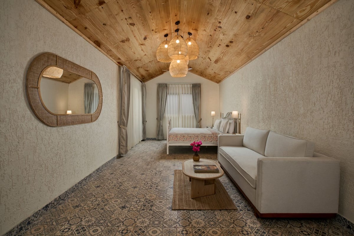 A cozy room with a wooden ceiling, a bed, a sofa, and a mirror.