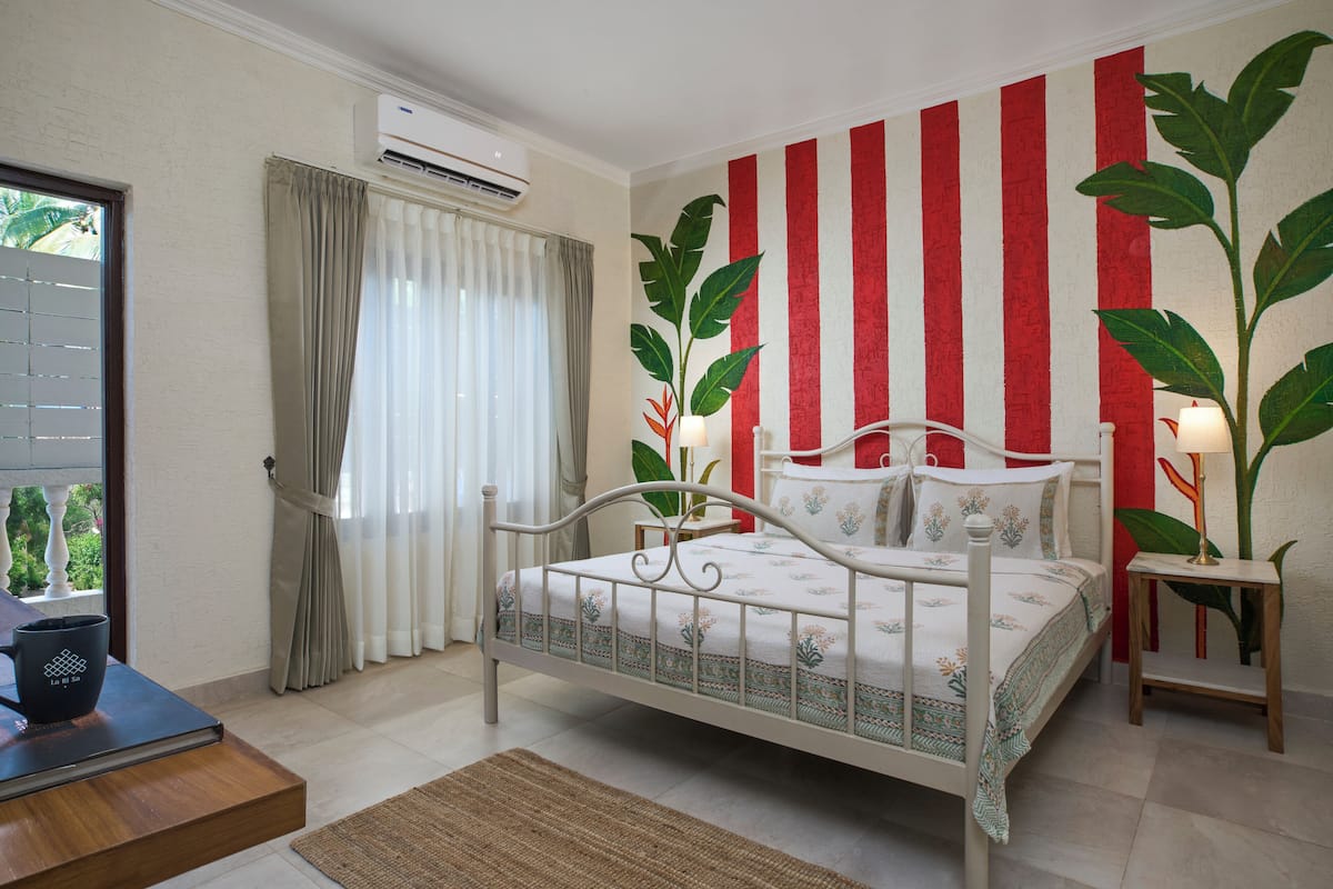 A bedroom with a bed, curtains, a window, an air conditioner, and a plant.