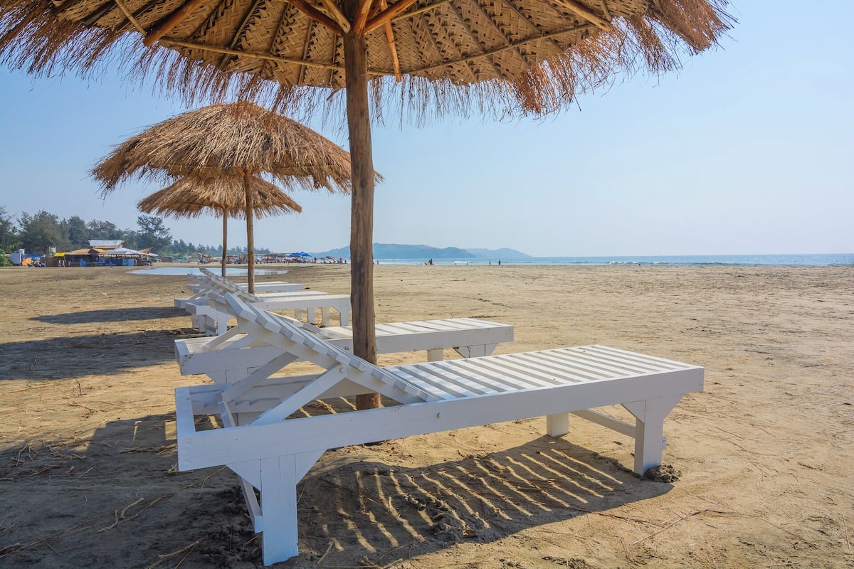 A beach with white lounge chairs and thatched umbrellas.