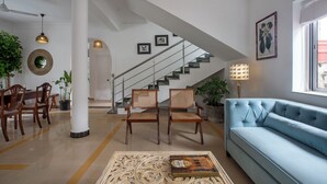 A spacious living room with a blue sofa, wooden chairs, a dining table, and a staircase leading to another level. - Larisa Resort, Morjim (Morjim)