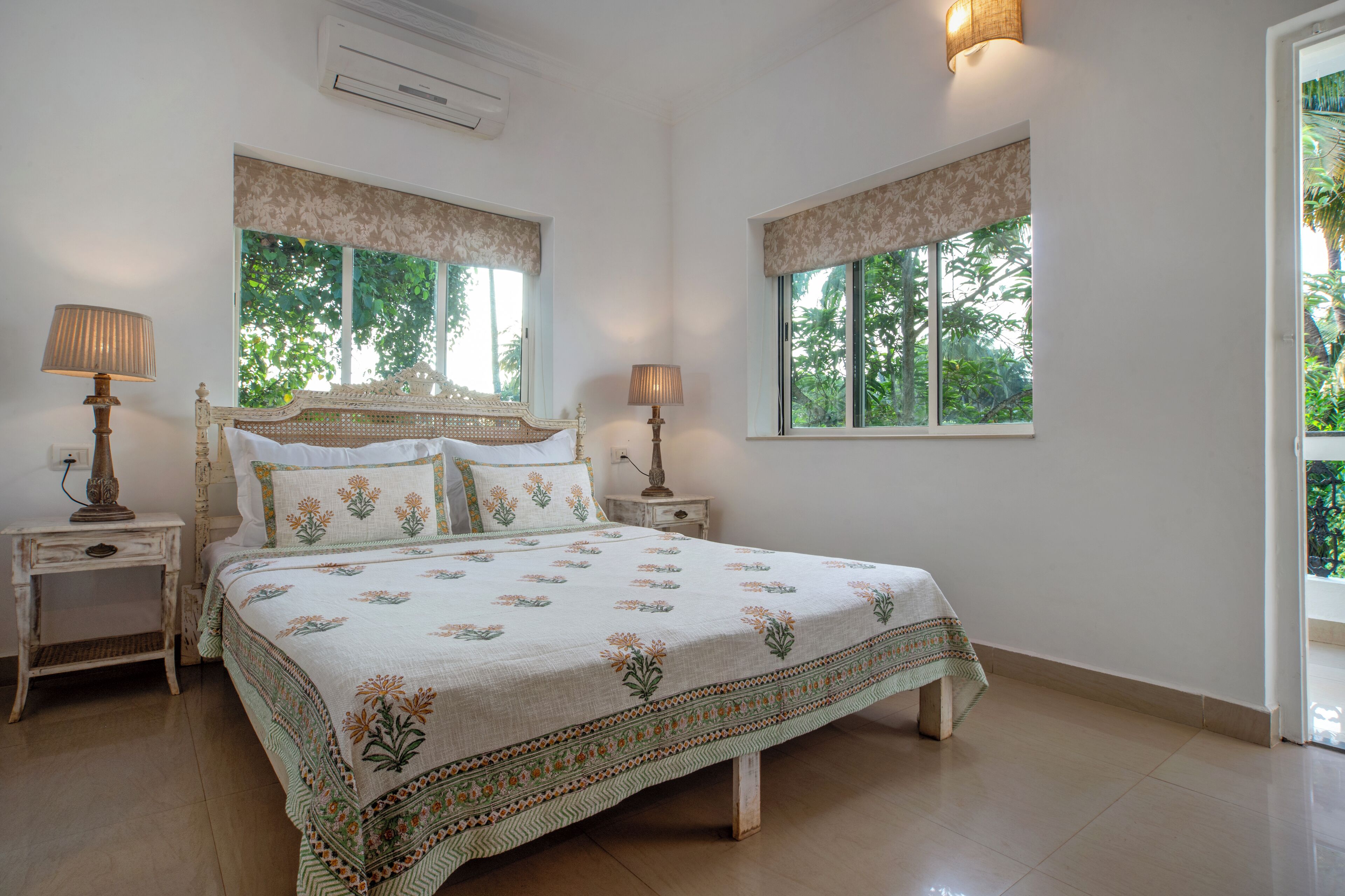 A bedroom with a large bed, two bedside tables, and two windows with curtains.