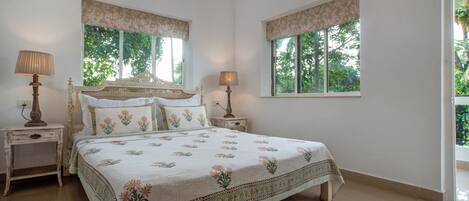 A bedroom with a large bed, two bedside tables, and two windows with curtains.