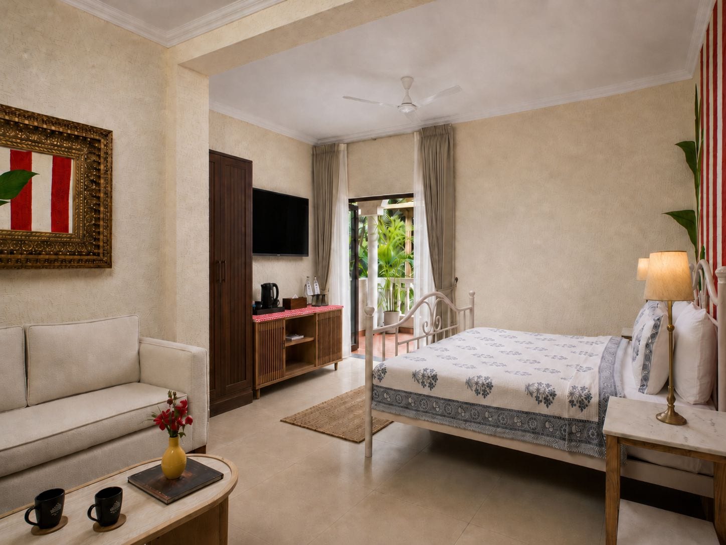 A hotel room with a bed, a sofa, a TV, a desk with a lamp, and a view of the outdoors.