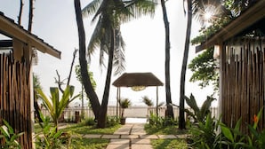 A pathway leading to a beach with palm trees and a thatched structure. - Larisa Resort, Morjim (Morjim)