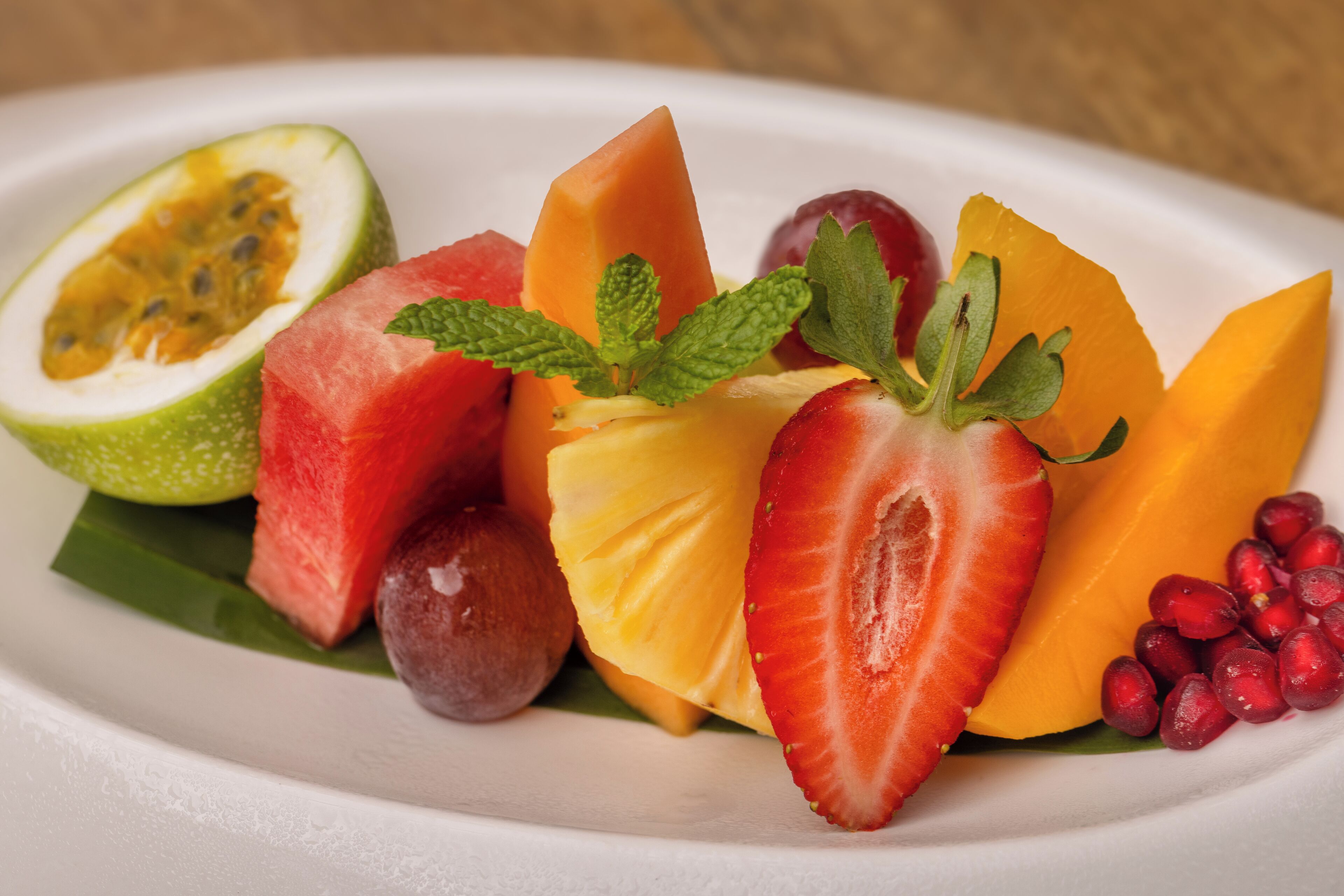 Un plat amb una varietat de fruites, com síndria, mango, pinya i melagrana.
