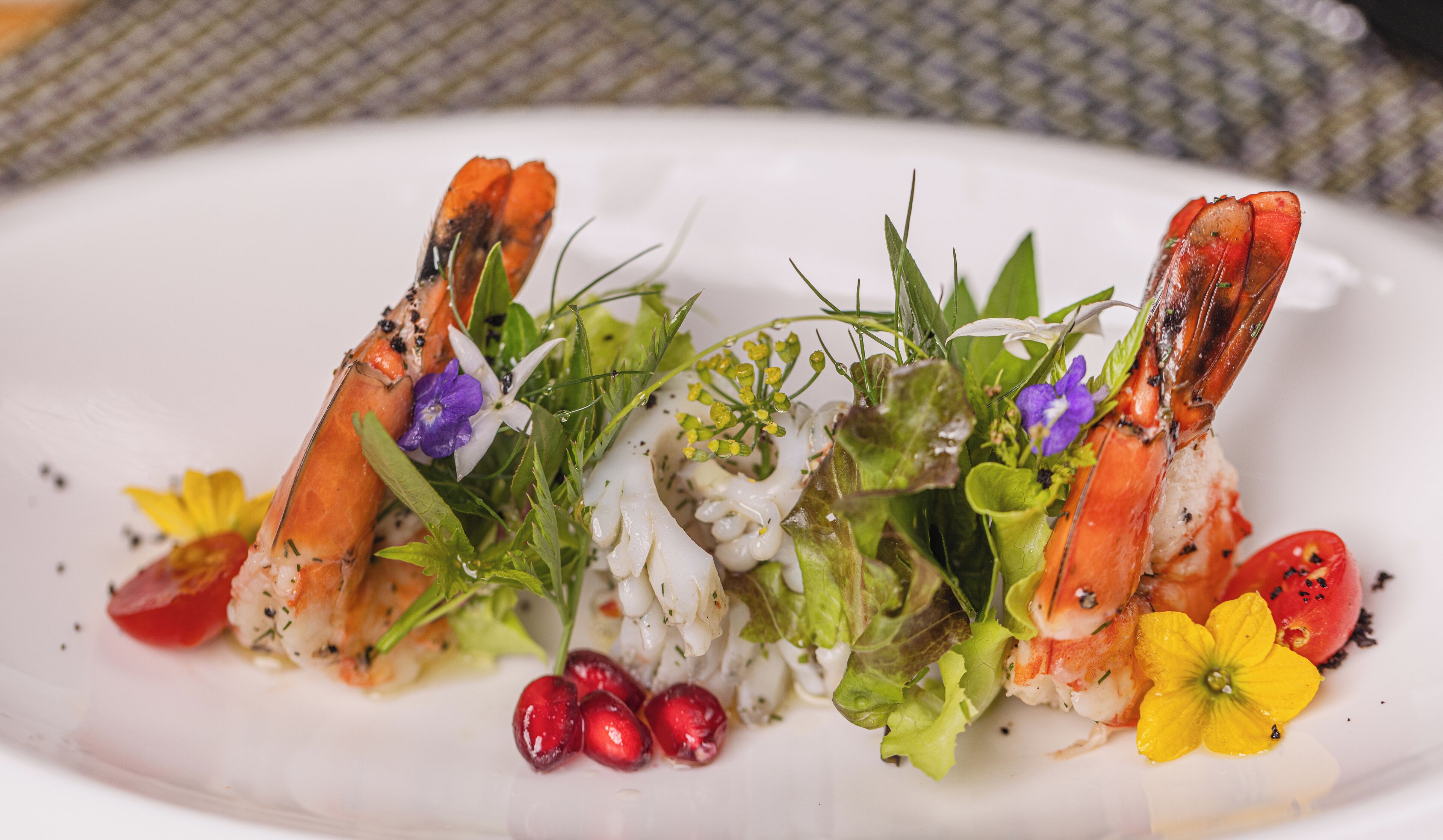 A plate of food with lobster tails, greens, and flowers.