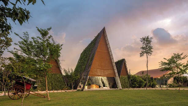 Un bâtiment moderne doté d’un toit triangulaire au design original, entouré d’une pelouse bien entretenue et d’arbres.
