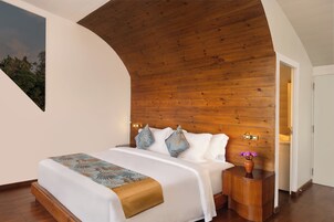 Un dormitorio moderno con techo de madera, una cama grande con ropa de cama estampada y una mesita de noche con un jarrón de flores.
