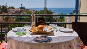 Une table dressée pour un repas sur un balcon, avec vue sur la mer et les bâtiments.
