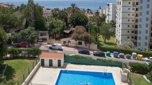 Une piscine avec vue sur la mer, entourée de verdure et d’immeubles d’habitation.