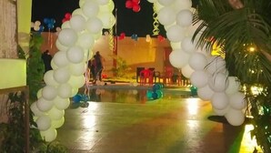 Un espacio al aire libre con un arco de globos blancos, una piscina y algo de vegetación.