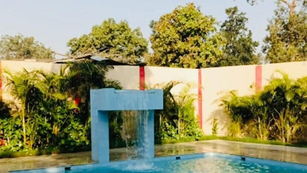 Una piscina rectangular con caída de agua, rodeada por un solado de azulejos y abundante vegetación.