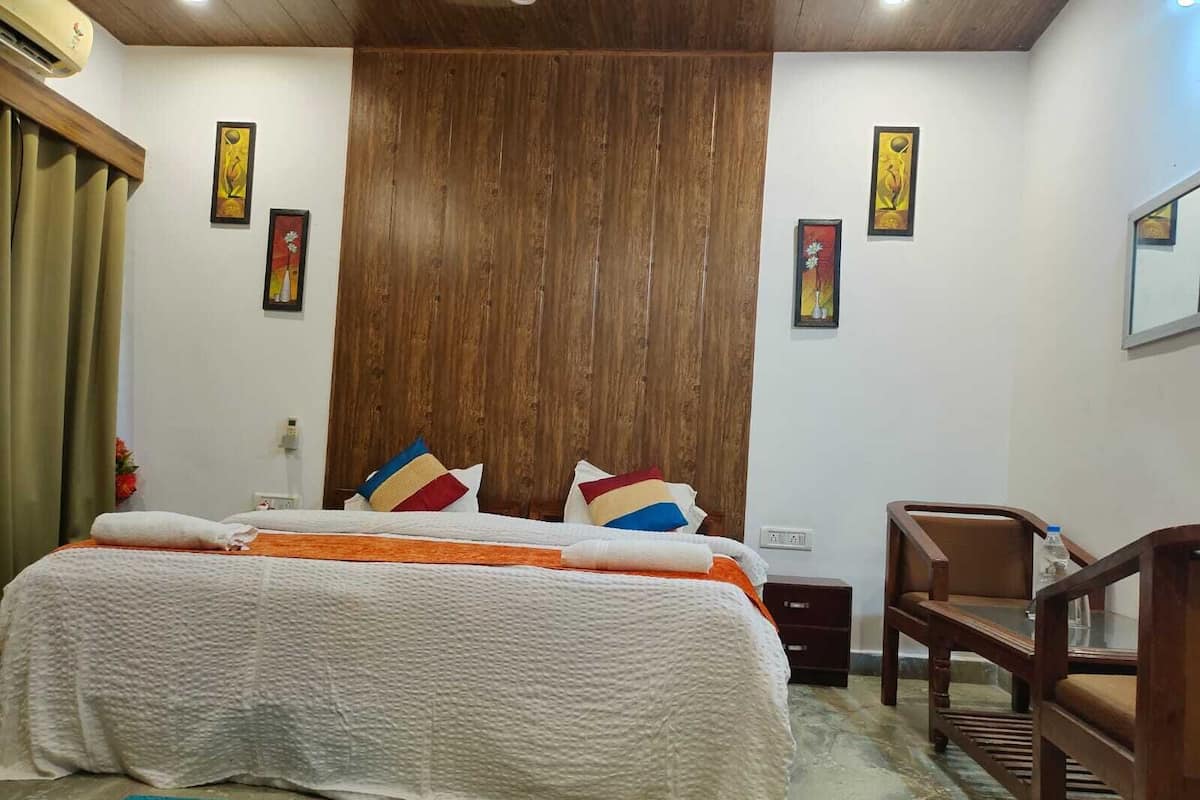 A bedroom with a wooden headboard, a bed with a white textured bedspread, colorful pillows, a wooden chair, and artwork on the walls.