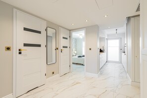 A hallway with white doors, a marble floor, and a view into a bedroom with a bed and a nightstand. - St.george (Antibes)