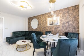 Uma sala moderna com um sofá modular verde escuro, uma mesa de centro redonda e um espaço de jantar com mesa branca para quatro pessoas.