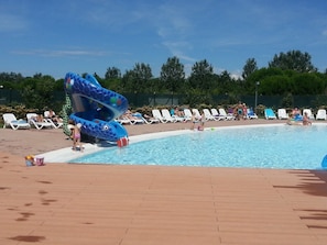 Una piscina con tobogán azul, sillas de descanso y una terraza de madera.