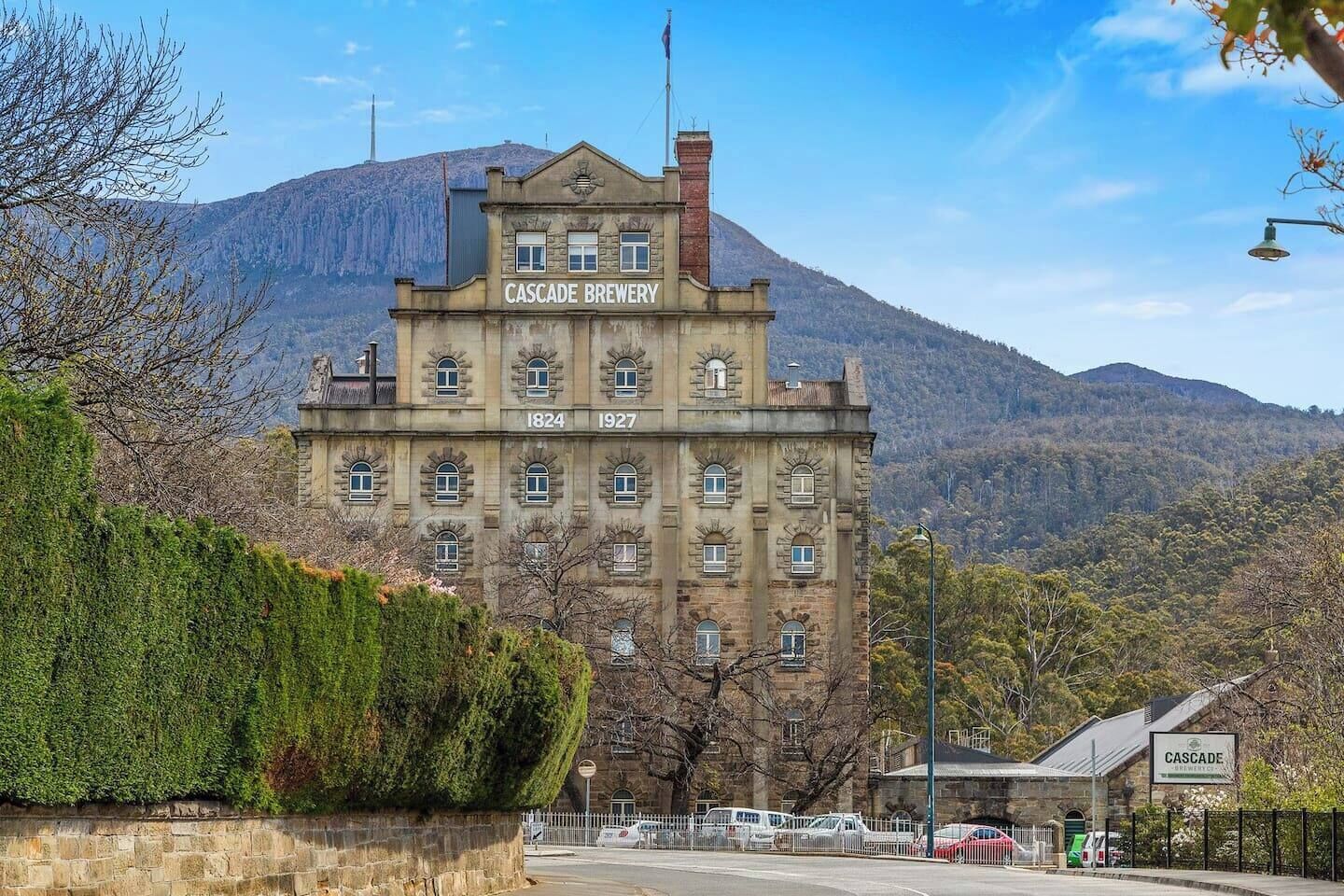 Een historisch gebouw met de aanduiding 'Cascade Brewery' en de jaren 1824 en 1927, omgeven door een bergachtig landschap.