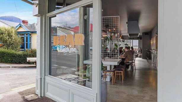 A restaurant with a large window displaying the name "BEAR with me". Inside, there are tables and chairs arranged for dining. - Explore South Hobart Village from an 1855 Cottage (Dynnyrne)
