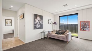 A modern living room with a beige sofa, a coffee table, and artwork on the walls. - Beachside Luxury Villa Expansive Panoramic Vistas (Kingston Beach)