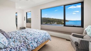 A bedroom with a bed, a chair, and large windows offering a view of the sea and hills. - Beachside Luxury Villa Expansive Panoramic Vistas (Kingston Beach)