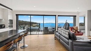 A modern living room with a large sliding glass door leading to a balcony with a sea view. - Beachside Luxury Villa Expansive Panoramic Vistas (Kingston Beach)