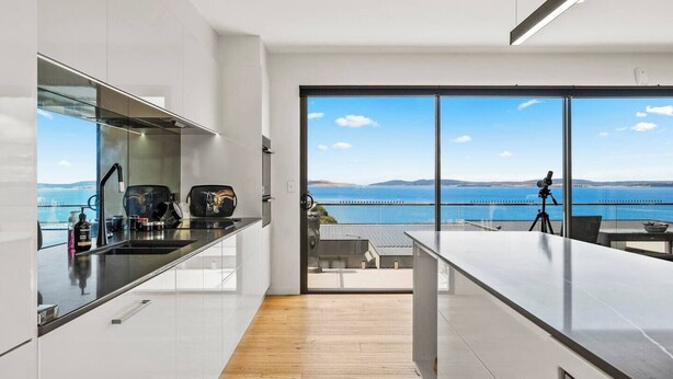 A modern kitchen with a large window overlooking a scenic view of the sea. - Beachside Luxury Villa Expansive Panoramic Vistas (Kingston Beach)