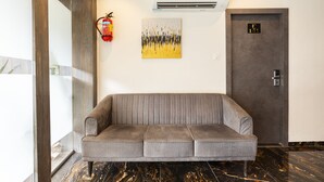 A modern lobby with a grey sofa, a fire extinguisher, an air conditioning unit, and a door marked with the number 101. - Hotel Classio Andheri (Mumbai)