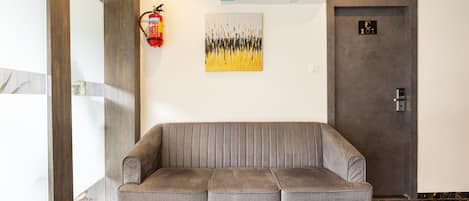 A modern lobby with a grey sofa, a fire extinguisher, an air conditioning unit, and a door marked with the number 101.