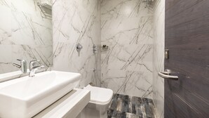 A bathroom with a marble wall, a white sink, a toilet, and a shower area. - Hotel Classio Andheri (Mumbai)