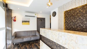 A modern reception area with a marble reception desk, a grey sofa, a fire extinguisher, and a wall-mounted clock. - Hotel Classio Andheri (Mumbai)