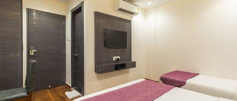 A hotel room with a bed, a chair, a television mounted on the wall, and an air conditioning unit.
