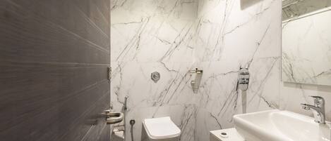Un baño con pared de mármol, inodoro, lavamanos y ducha.