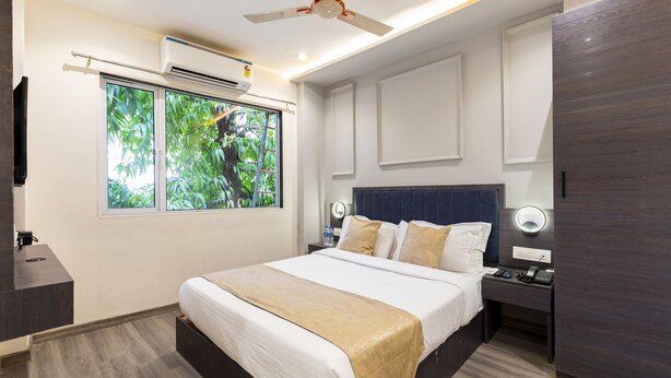 A modern hotel room with a large bed, bedside tables, a ceiling fan, and a window with a view of greenery. - Hotel Classio Andheri (Mumbai)