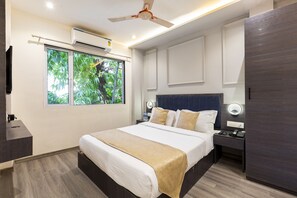 A modern hotel room with a large bed, bedside tables, a ceiling fan, and a window with a view of greenery. - Hotel Classio Andheri (Mumbai)