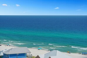 A beach view with clear skies, a calm sea, and a few buildings in the foreground.