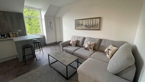 A modern living room with a grey sofa, a coffee table, and a kitchen area with a bar stool. - Crown àros beag, ultra central, 2-bedroom, 2nd floor apartment.

 (Inverness)