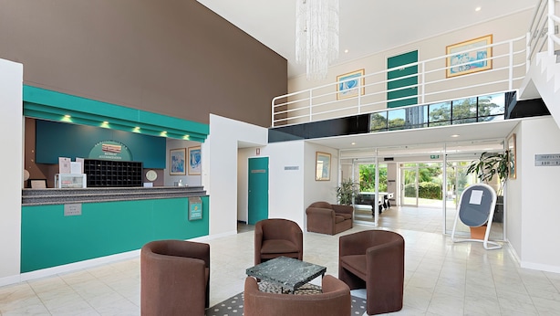 Een moderne lobby met een receptiebalie, een zithoek en een trap naar een hoger gelegen verdieping.