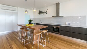 A modern kitchen with a wooden island, bar stools, a fish mounted on the wall, and a large stove. - On The Beach (Lorne)
