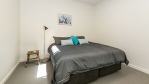 A bedroom with a bed, a floor lamp, a small wooden stool, and a framed picture on the wall. - On The Beach (Lorne)