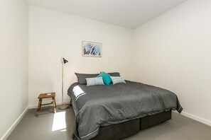 Ein Schlafzimmer mit einem Bett, einer Stehlampe, einem kleinen Holzschemel und einem gerahmten Bild an der Wand.